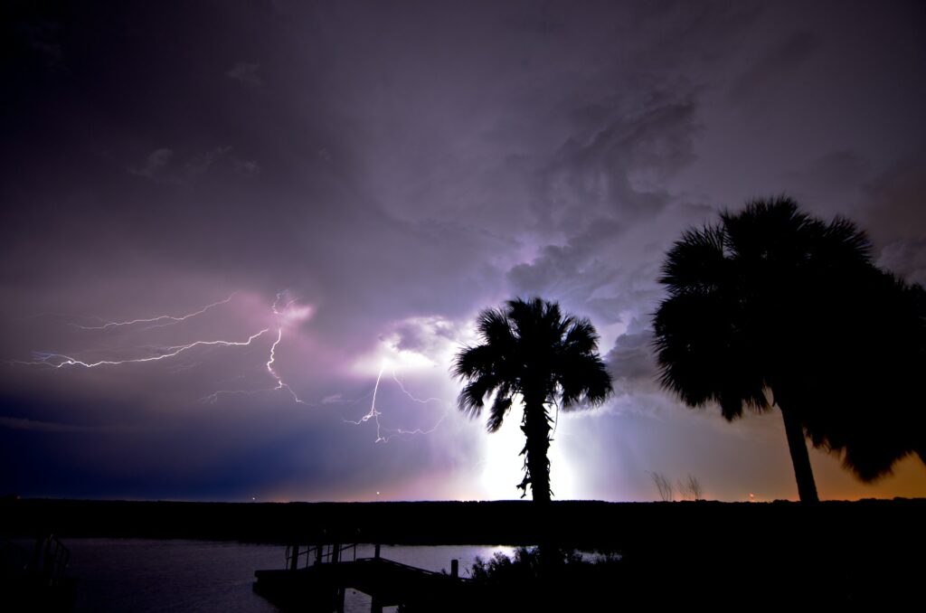 Lightning illuminates a purple sky, palm trees and the water at the St. Johns River west of Cocoa,